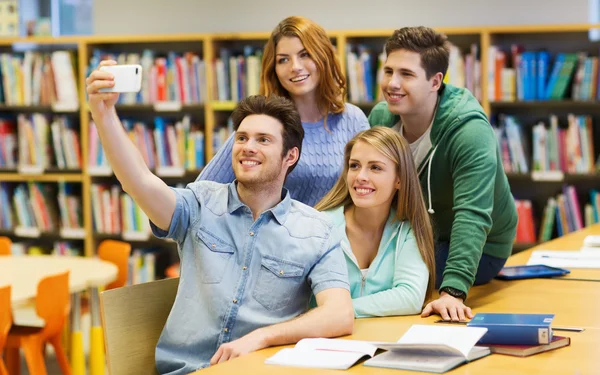 Estudantes com smartphone tirando selfie na biblioteca — Fotografia de Stock