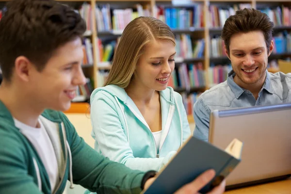 Estudantes felizes com laptop e livro na biblioteca — Fotografia de Stock