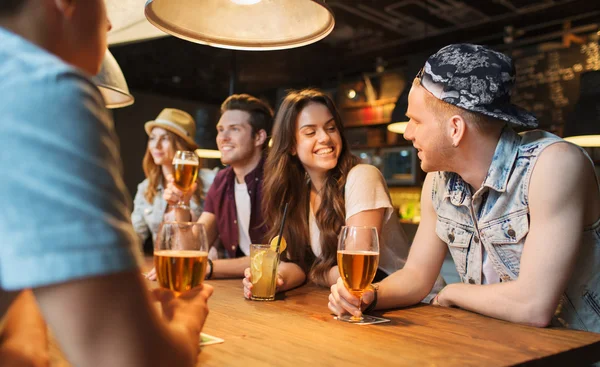 Happy friends with drinks talking at bar or pub — Stock Photo, Image