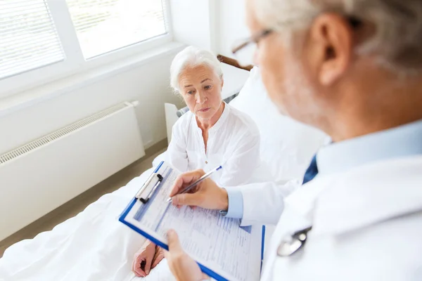 Seniorin und Arzt mit Klemmbrett im Krankenhaus — Stockfoto