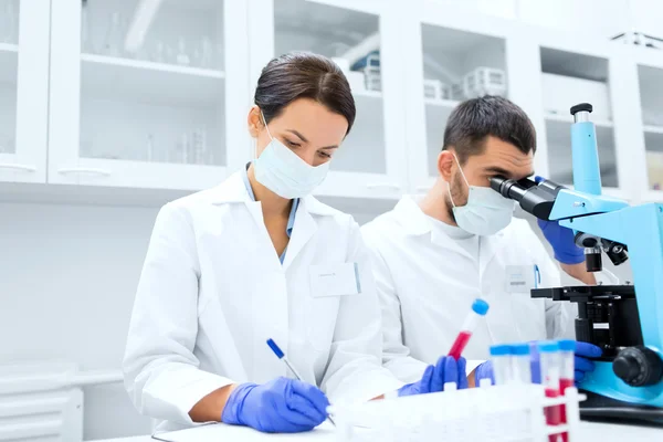 Científicos con portapapeles y microscopio en laboratorio —  Fotos de Stock