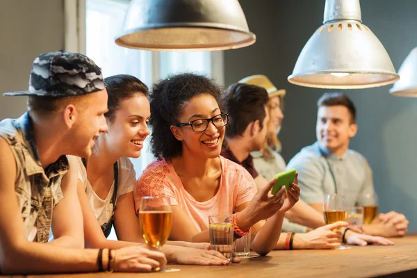 Happy friends with smartphone and drinks at bar — Stock Fotó