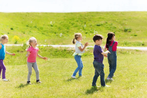 Grupo de crianças pegando bolhas de sabão ao ar livre — Fotografia de Stock