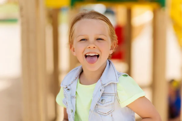 Счастливая маленькая девочка, показывающая язык на детской площадке — стоковое фото