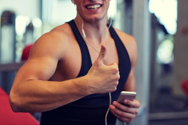 Hombre feliz con teléfono inteligente y auriculares en el gimnasio —  Fotos de Stock