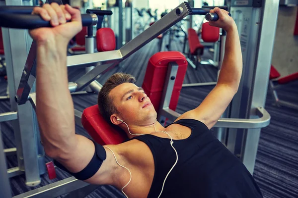 Young man with earphones exercising on gym machine — Stock Photo, Image