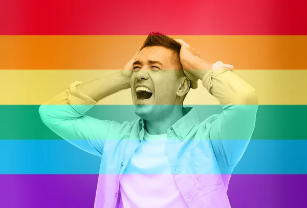 Unhappy gay man shouting over rainbow flag — ストック写真