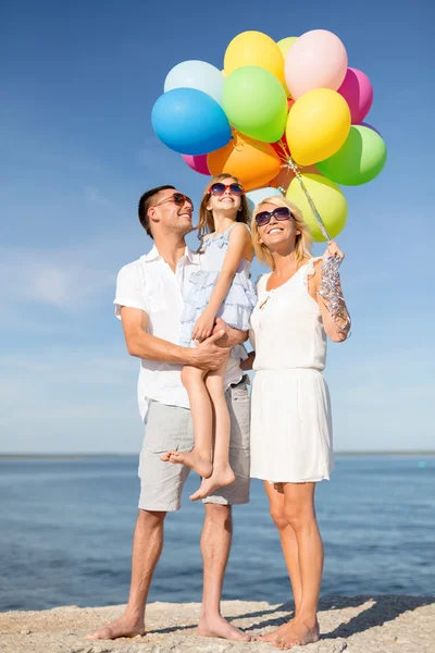 Glückliche Familie mit bunten Luftballons am Meer — Stockfoto