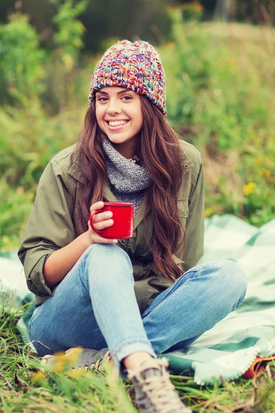 Sonriente joven mujer con taza sentado en camping — Foto de Stock