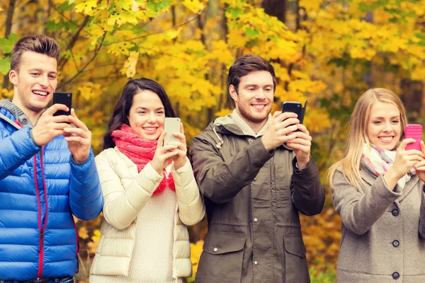 Amis souriants avec smartphones dans le parc de la ville — Photo