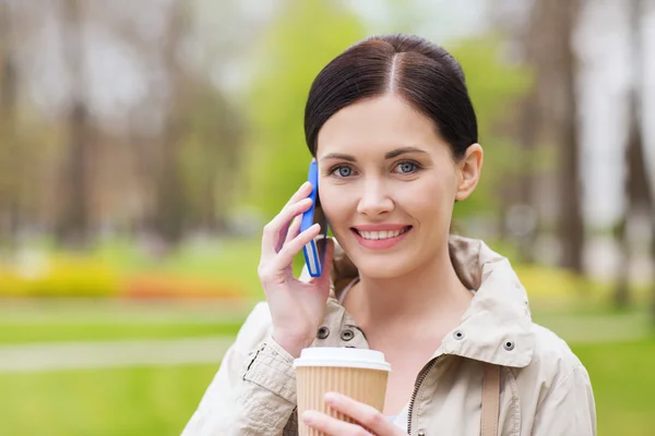 Lachende vrouw met smartphone en koffie in park — Stockfoto