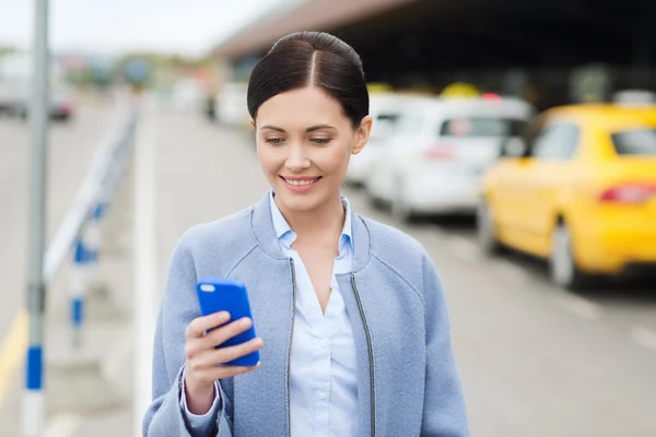 Usmívající se žena s smartphone za taxi v městě — Stock fotografie