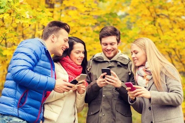 Amis souriants avec smartphones dans le parc de la ville — Photo