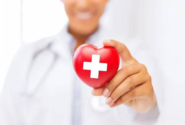 Female doctor holding heart with red cross symbol — Stock Photo, Image