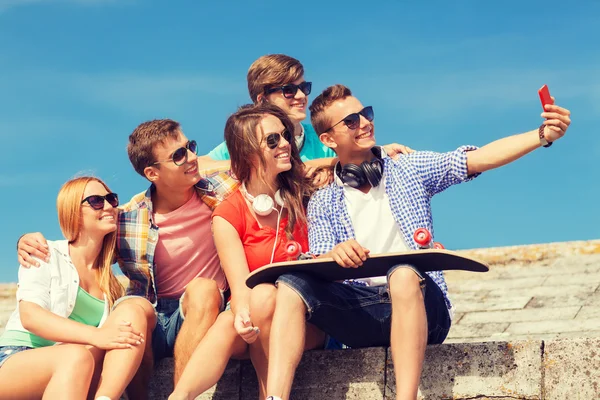 Группа улыбающихся друзей со смартфоном на открытом воздухе — стоковое фото