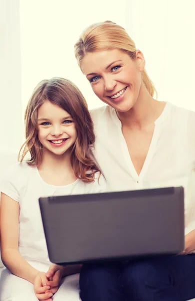 Улыбающаяся мать и маленькая девочка с ноутбуком дома — стоковое фото