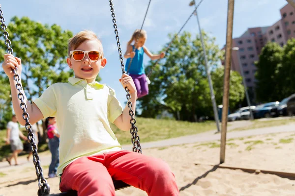Två glada barn svängande på swing på lekplats — Stockfoto