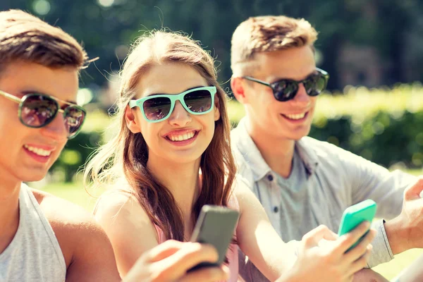Usmívající se přátelé s smartphone sedí v parku — Stock fotografie