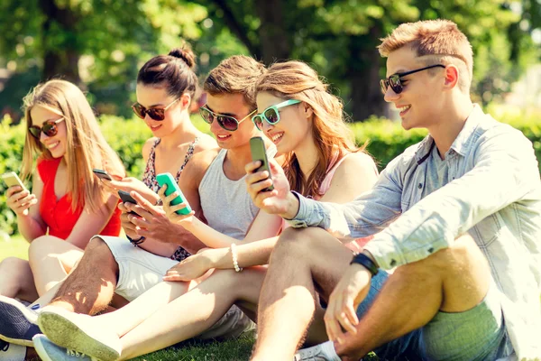 Χαμόγελο φίλοι με smartphones που κάθεται στο γρασίδι — Φωτογραφία Αρχείου