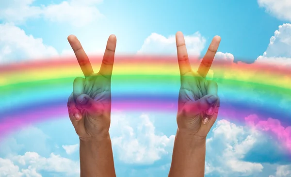 Hands showing peace sign over rainbow in sky — Stock Photo, Image