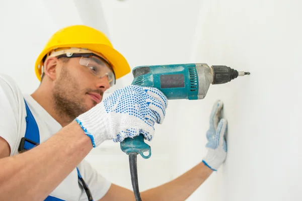 Builder in hardhat with drill perforating wall — Stock Photo, Image