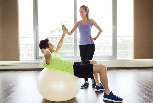 Sonriente hombre y mujer con bola de ejercicio en el gimnasio —  Fotos de Stock