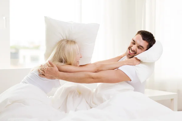 Feliz pareja teniendo almohada lucha en cama en casa —  Fotos de Stock