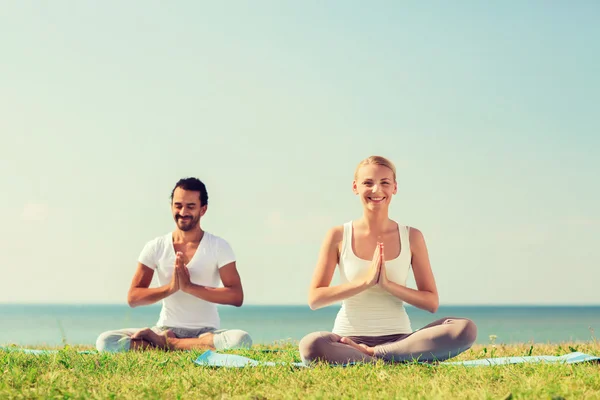 Sorrindo casal fazendo exercícios de ioga ao ar livre — Fotografia de Stock