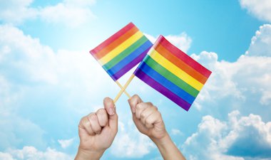 hands holding rainbow flags over sky background clipart