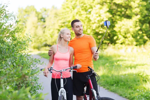 Casal com bicicleta e vara selfie smartphone — Fotografia de Stock