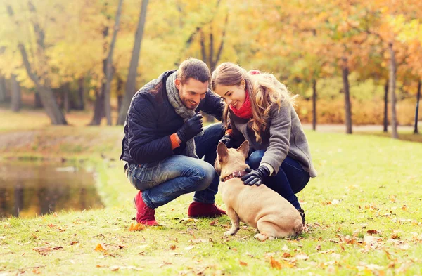 Улыбающаяся пара с собакой в осеннем парке — стоковое фото