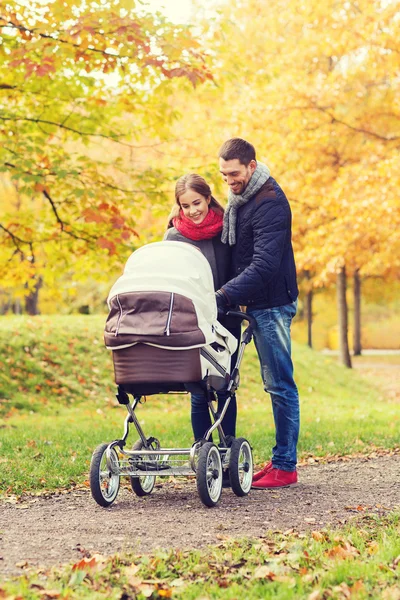 Pareja sonriente con cochecito de bebé en el parque de otoño —  Fotos de Stock