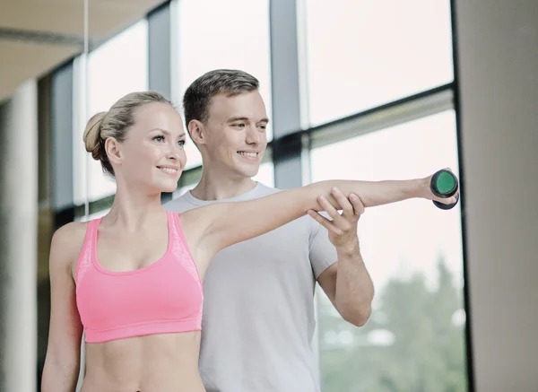 Smiling young woman with personal trainer in gym — Stock Photo, Image