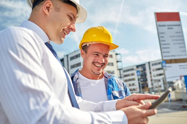 Construtores felizes em hardhats com tablet pc ao ar livre — Fotografia de Stock