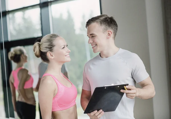 Sorrindo jovem mulher com personal trainer no ginásio — Fotografia de Stock