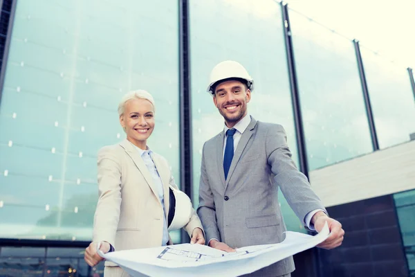 Hombres de negocios sonrientes con planos y cascos — Foto de Stock