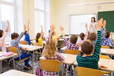 group of school kids raising hands in classroom clipart