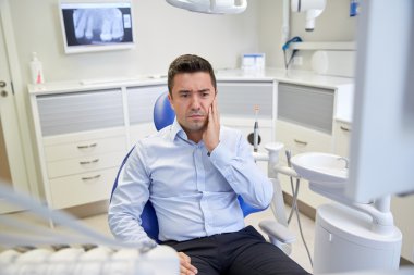 man having toothache and sitting on dental chair clipart