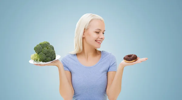 Mujer sonriente con brócoli y donut — Foto de Stock