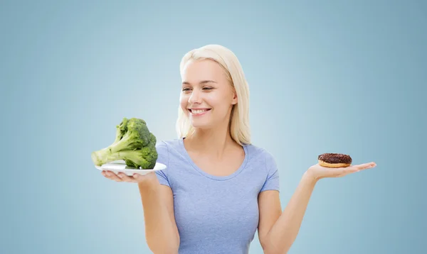 Mulher sorridente com brócolis e donut — Fotografia de Stock