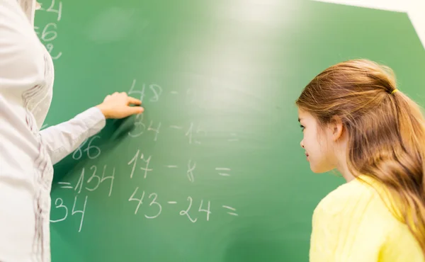 Schoolgirl and teacher with task on chalk board — 图库照片