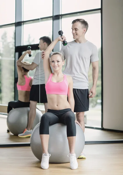 Smiling young woman with personal trainer in gym — Stock Photo, Image