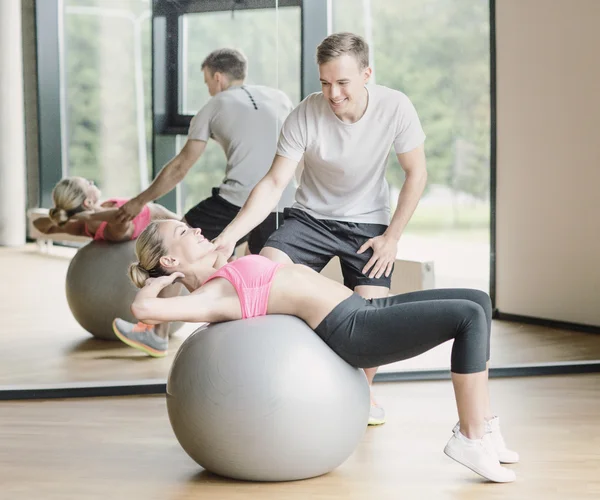 Leende ung kvinna med personlig tränare i gym — Stockfoto