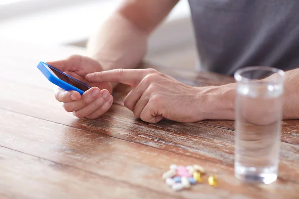 Close up of hands with smartphone, pills and water — Stock Photo, Image