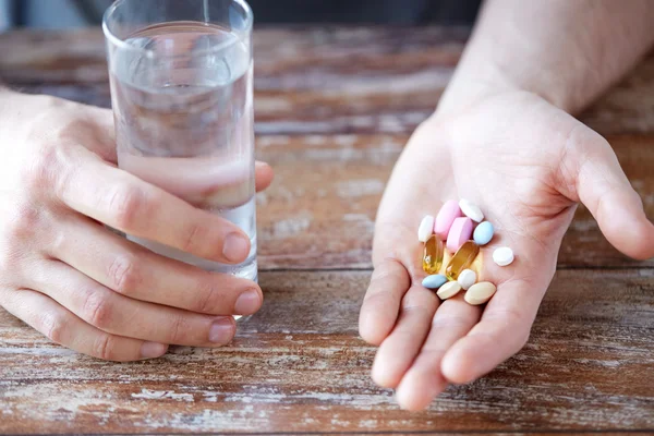 Primer plano de manos masculinas sosteniendo píldoras y agua — Foto de Stock