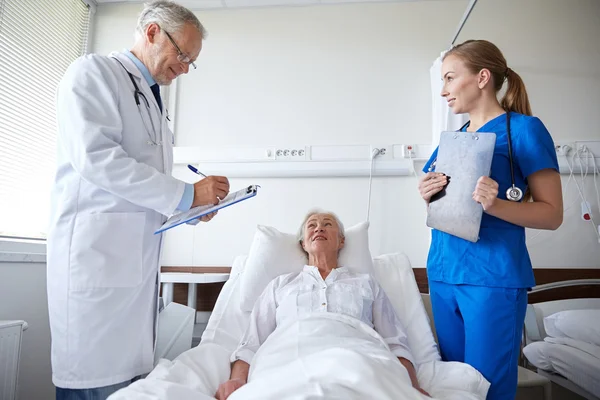 Médico e enfermeira visitando mulher idosa no hospital — Fotografia de Stock