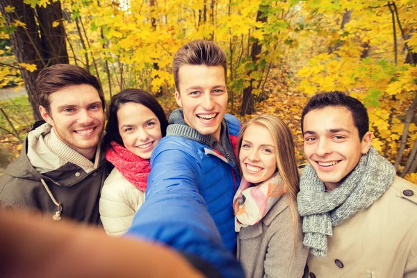 Группа улыбающихся мужчин и женщин в осеннем парке — стоковое фото