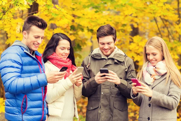 Amigos sorridentes com smartphones no parque da cidade — Fotografia de Stock