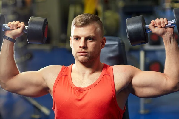 Joven con mancuernas flexionando los músculos en el gimnasio —  Fotos de Stock