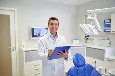 happy male dentist with clipboard at dental clinic clipart